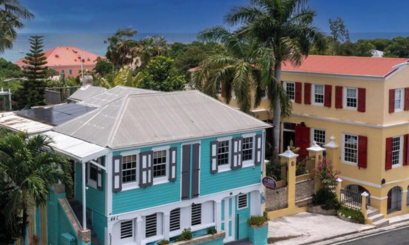 A turquoise building with a red roof, white shutters, and a balcony.