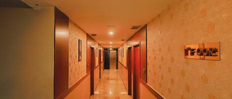 Un pasillo de hotel con puertas, un papel tapiz decorativo y un cartel.
