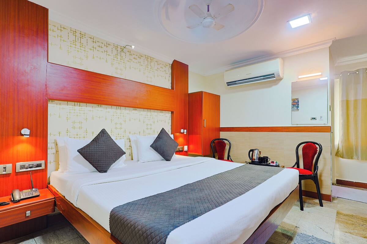 Una habitación de hotel con cama, mesita de noche, sillas y un equipo de aire acondicionado.