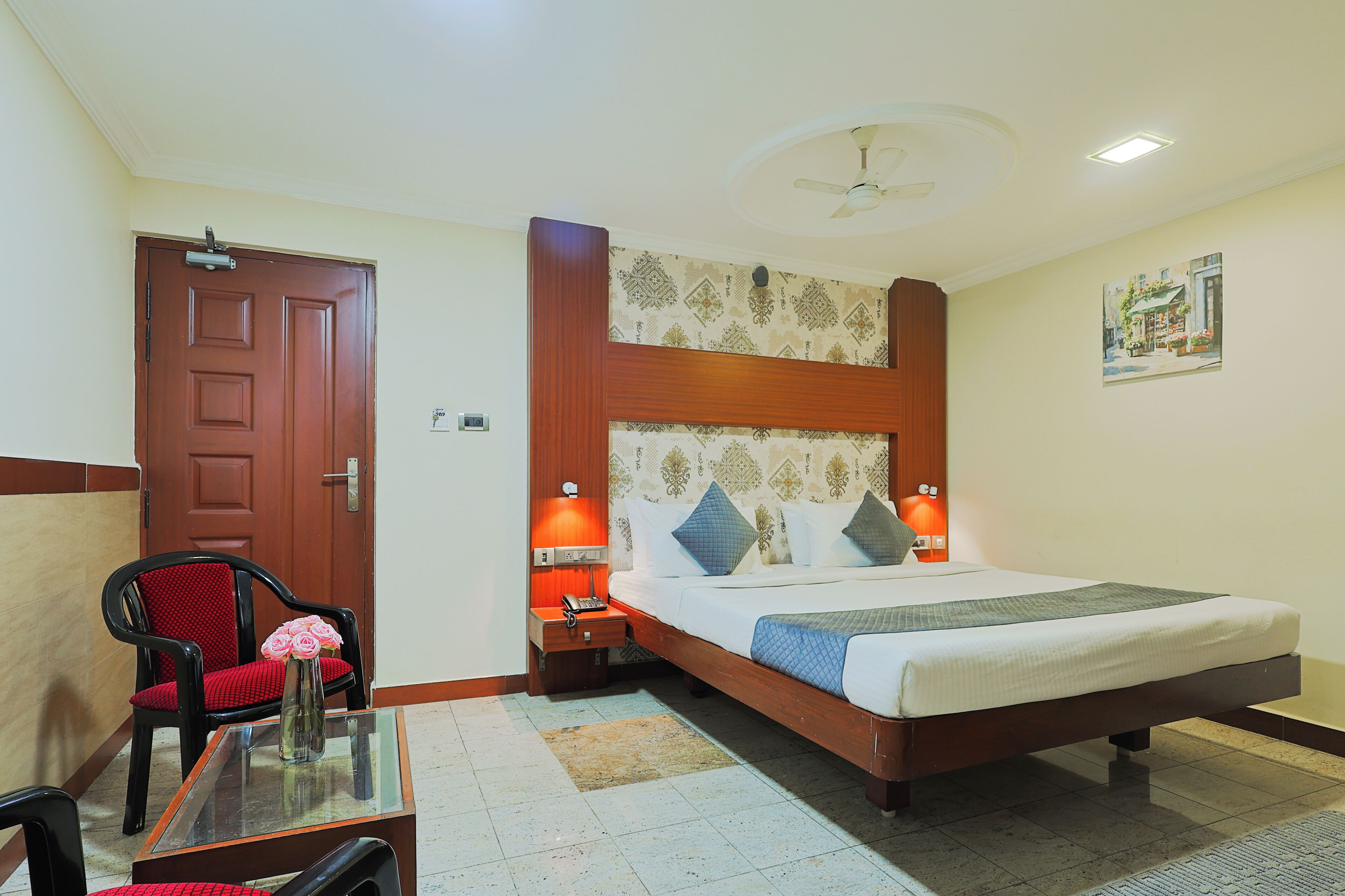 A hotel room with a bed, a chair, a nightstand, a table, and a ceiling fan.