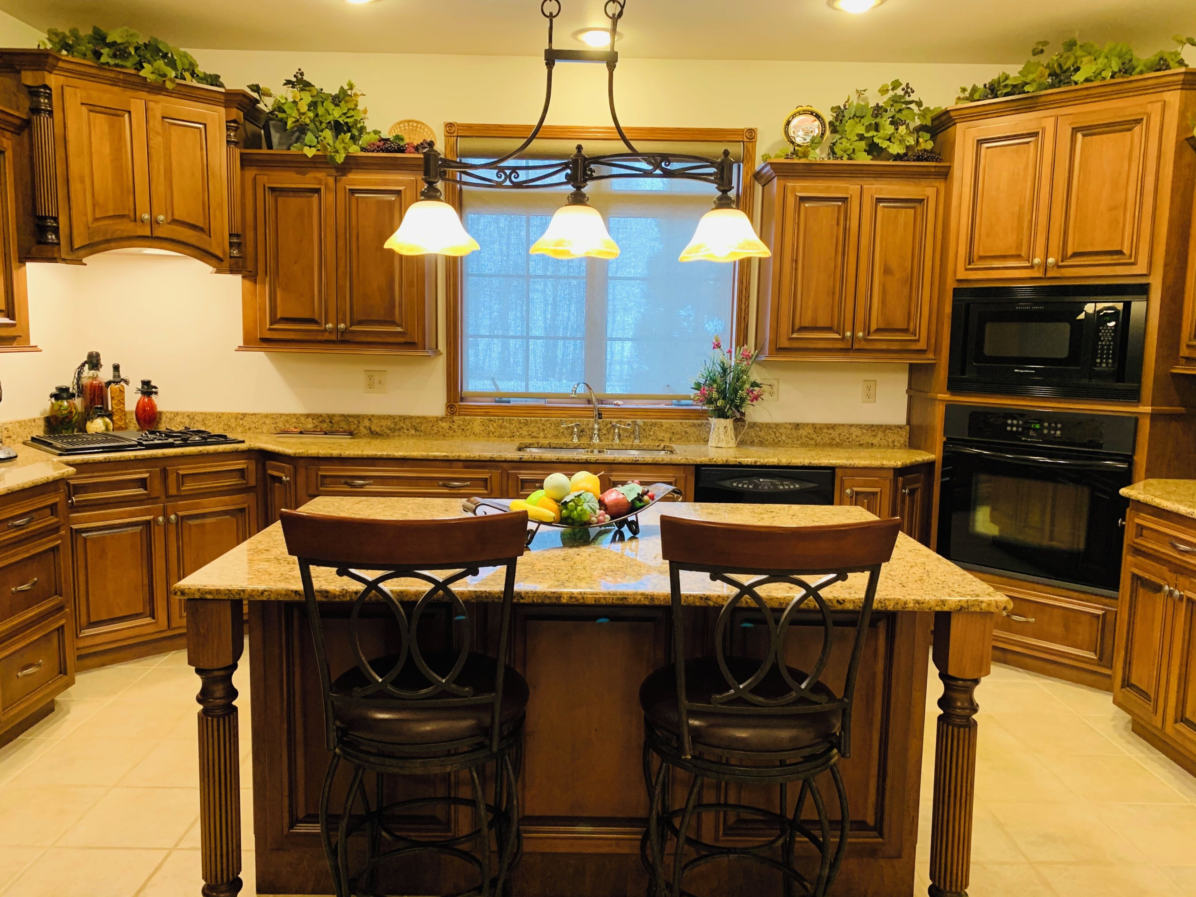 A kitchen with wooden cabinets, a granite countertop, a central island with chairs, and a window above the sink.