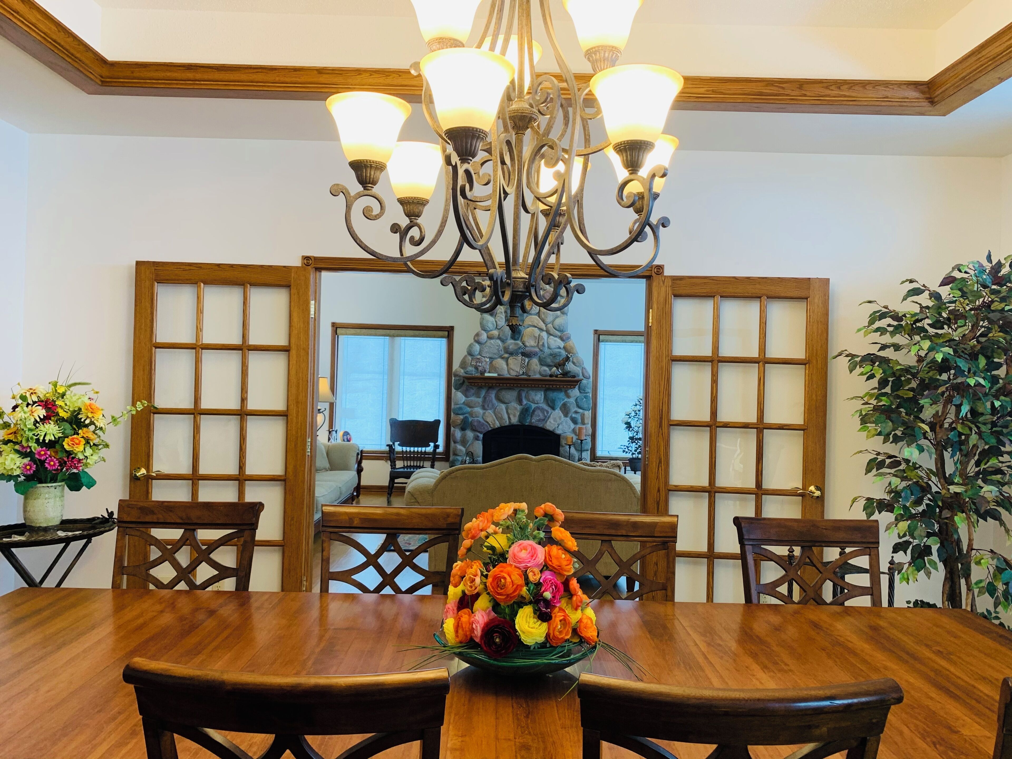 A dining area with a wooden table, chairs, a chandelier, and a stone fireplace.