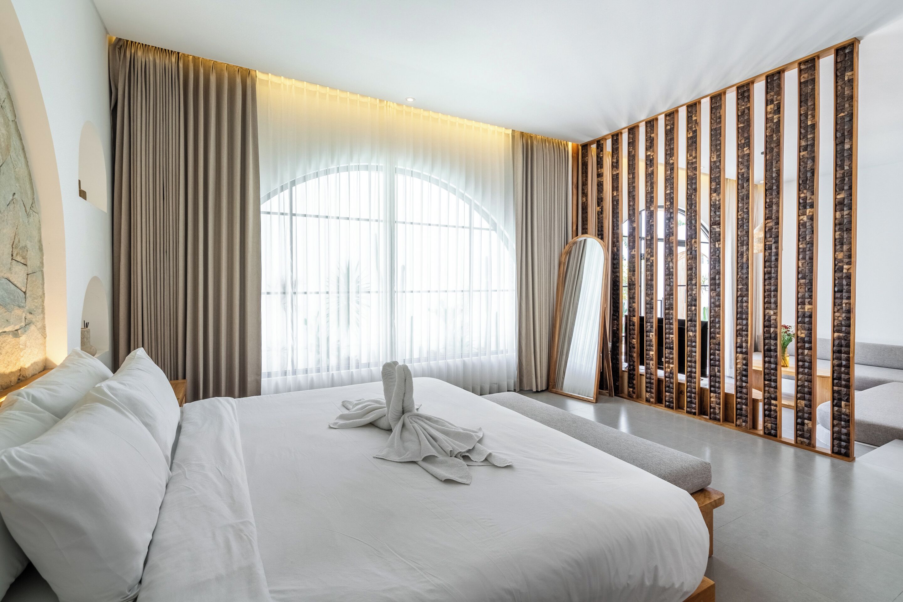Une chambre d’hôtel moderne avec un grand lit, un miroir et une vue sur la ville par la fenêtre.