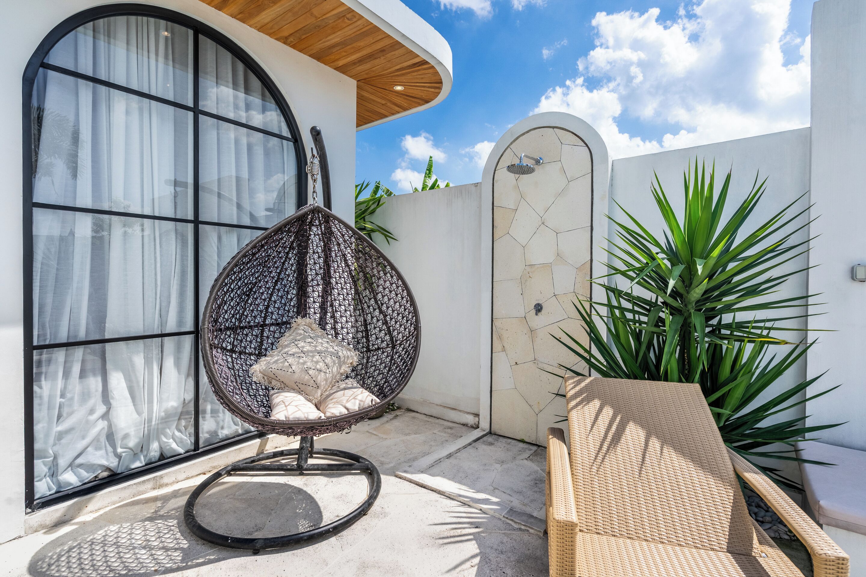Un espace extérieur moderne aménagé avec des sièges, comprenant un fauteuil en osier, un fauteuil de relaxation et une grande plante en pot.