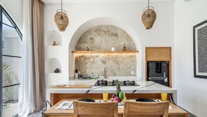 A modern kitchen with a stone backsplash, wooden cabinetry, and a dining area with two chairs. - TARRA VILLA by Exotic Bali Properties  (Canggu)