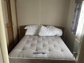 A single bed with striped bedding, a wooden wardrobe, and a window with curtains. - Hoburne Blue Anchor - Holiday Accommodation 18081 (Minehead)