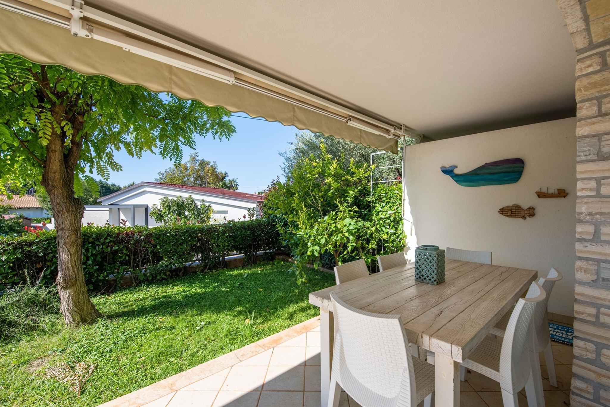 Eine überdachte Terrasse mit Tisch und Stühlen, ein Baum und ein Haus im Hintergrund.
