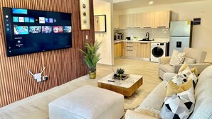 Un saló modern amb televisió de pantalla plana, un sofà, una taula de centre i una cuina al fons.