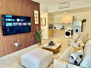 Ein modernes Wohnzimmer mit einem Flachbildfernseher, einer Couch, einem Couchtisch und einer Küche im Hintergrund.