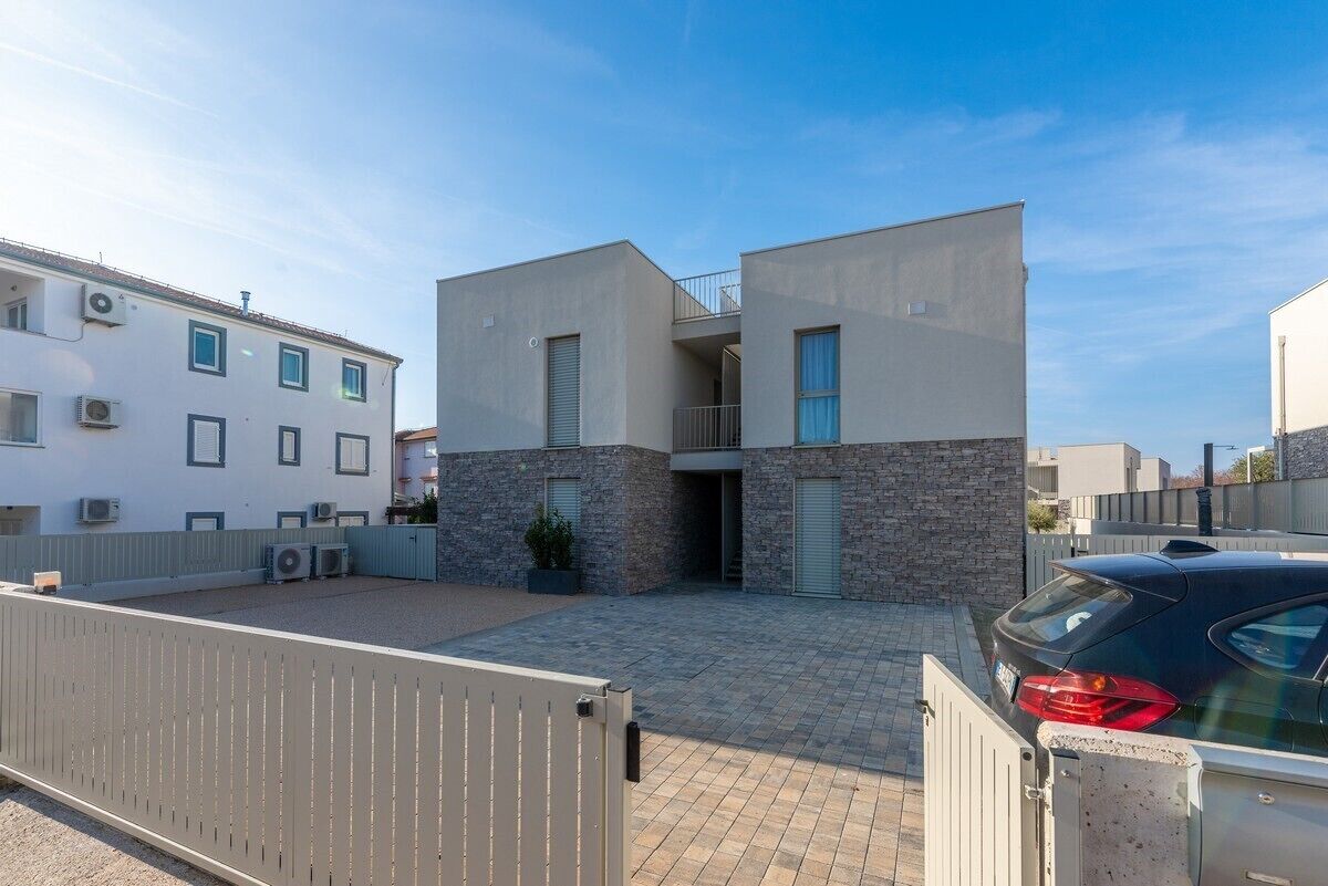 A modern two-story building with a stone facade, a balcony, and a gated entrance.
