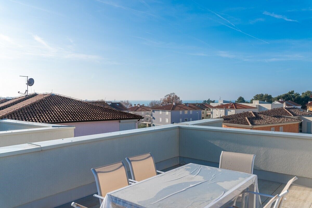 Une terrasse sur le toit, avec une table et des chaises, une antenne parabolique et une vue sur les maisons voisines.