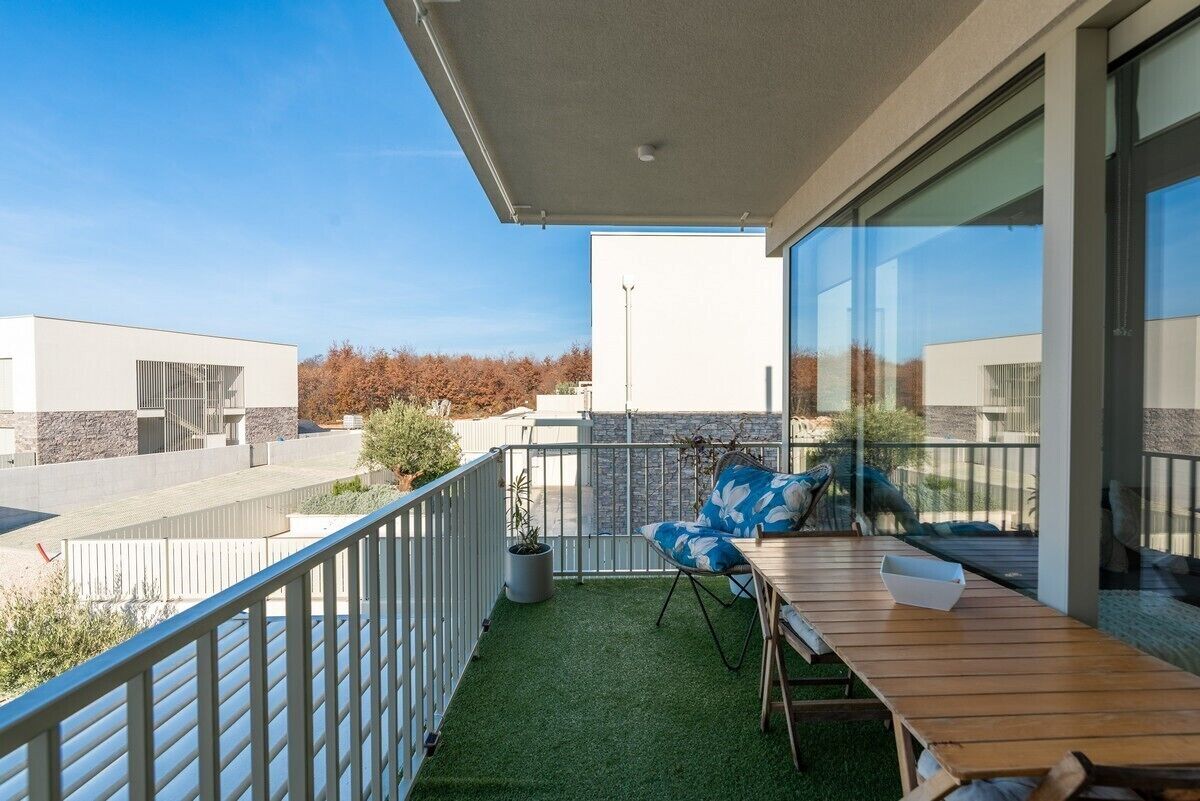 Un balcon avec une table et des chaises en bois, un pot de fleurs et une vue sur les immeubles.