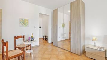 A room with a dining table, chairs, a mirror, a bedside table with a lamp, and artwork on the walls.