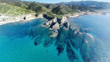 An aerial view of a coastal landscape with clear blue waters, rocky formations, and green hills.