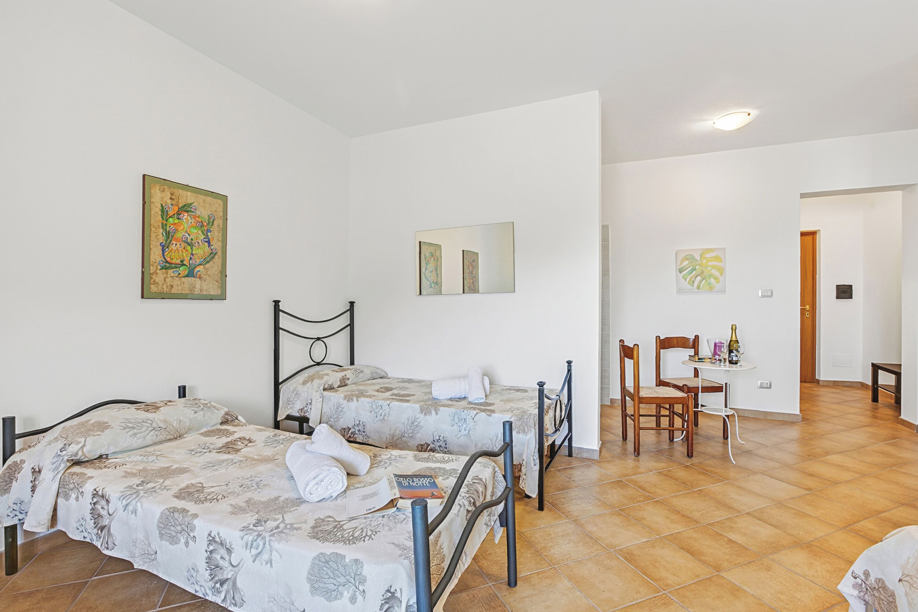 A room with two beds, a dining area with chairs and a table, and artwork on the walls.