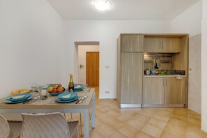 A dining area with a table set for two, a kitchen with wooden cabinets, and a hallway leading to a door.
