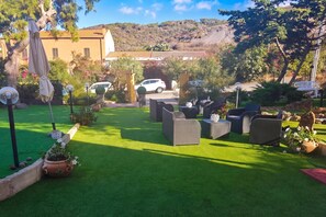 A well-maintained outdoor seating area with artificial grass, surrounded by potted plants and a view of a hillside.