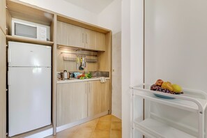 A compact kitchen with a microwave, refrigerator, and wooden cabinets.
