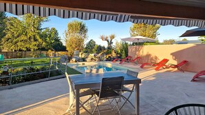 An outdoor pool area with lounge chairs, a table, and a view of trees and a rock formation. - Charmante maison avec piscine (Pomport)