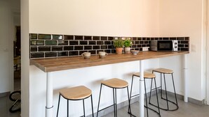 A kitchen with a wooden countertop, black and white backsplash, a microwave, and three stools. - Charmante maison avec piscine (Pomport)
