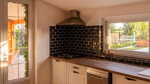 A kitchen with a black tiled backsplash, a stainless steel range hood, white cabinets, and a dishwasher. - Charmante maison avec piscine (Pomport)