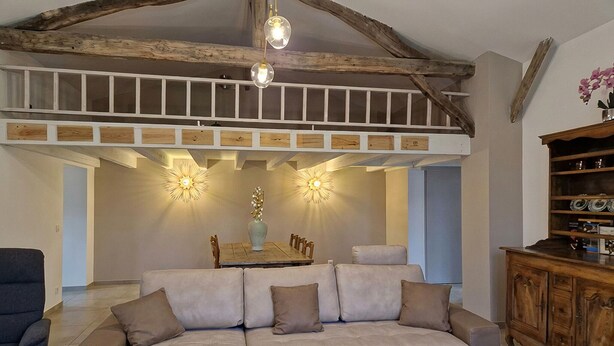 A spacious living area with a high ceiling, exposed wooden beams, a central dining table, and a sofa with cushions. - Charmante maison avec piscine (Pomport)