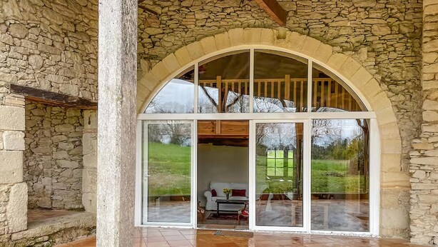 A stone archway leading to a room with a glass door, a tiled floor, and a view of a garden. - Belle maison avec piscine (Les Esseintes)