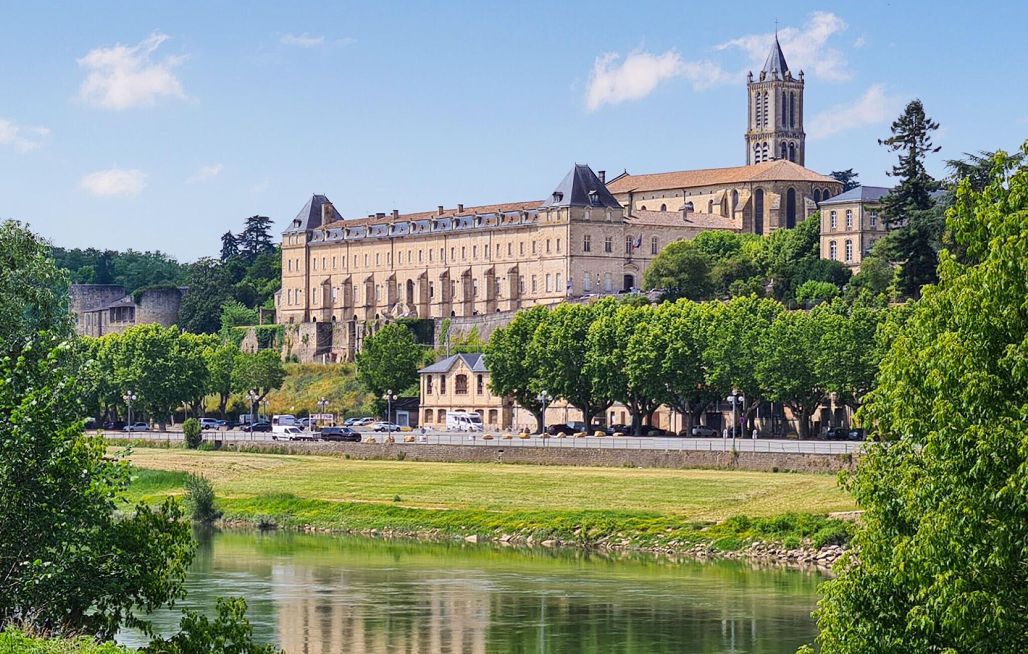 A historic building with a prominent tower, surrounded by lush greenery and a calm river.