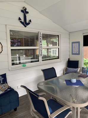 Un comedor con mesa de vidrio, sillas azules, pared blanca con ventana y un cartel que dice 'LAKEHOUSE'.