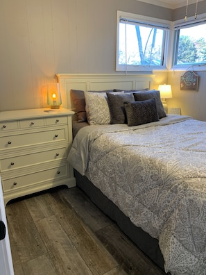 Un dormitorio con cama, mesita de noche, cómoda, ventana y un cartel en la pared.