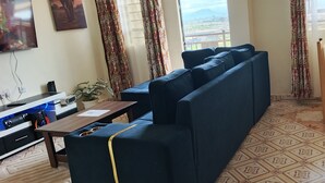 Ein Wohnzimmer mit einer Couch, einem Holztisch, einem Fernseher und Blick auf eine Landschaft durch das Fenster.