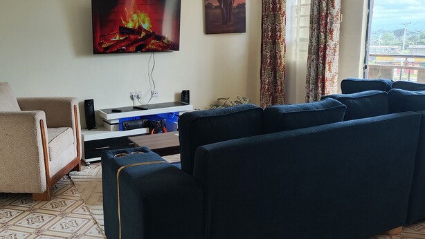 Ein Wohnzimmer mit einem beigefarbenen Sofa, einem blauen Sofa, einem Fernseher und einem Fenster mit Blick.