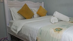 Ein Bett mit weißem Kopfteil, zwei Kissen, einem gerollten Handtuch und einer Bettdecke mit Blumenmuster.
