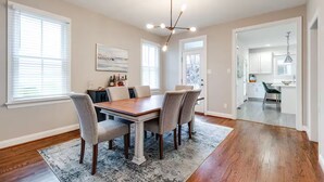 A dining area with a wooden table, four chairs, a chandelier, and a view into the kitchen.