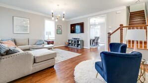 A spacious living room with a sofa, a blue chair, a white fluffy rug, and a wooden staircase.