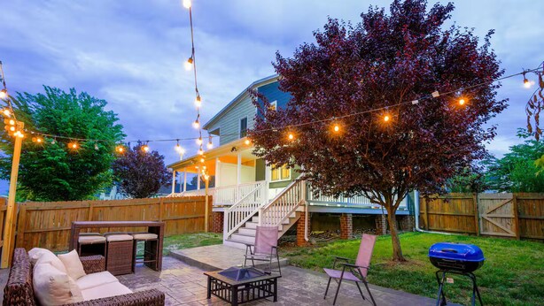 A backyard patio with outdoor furniture, a barbecue grill, and a staircase leading to a covered porch.
