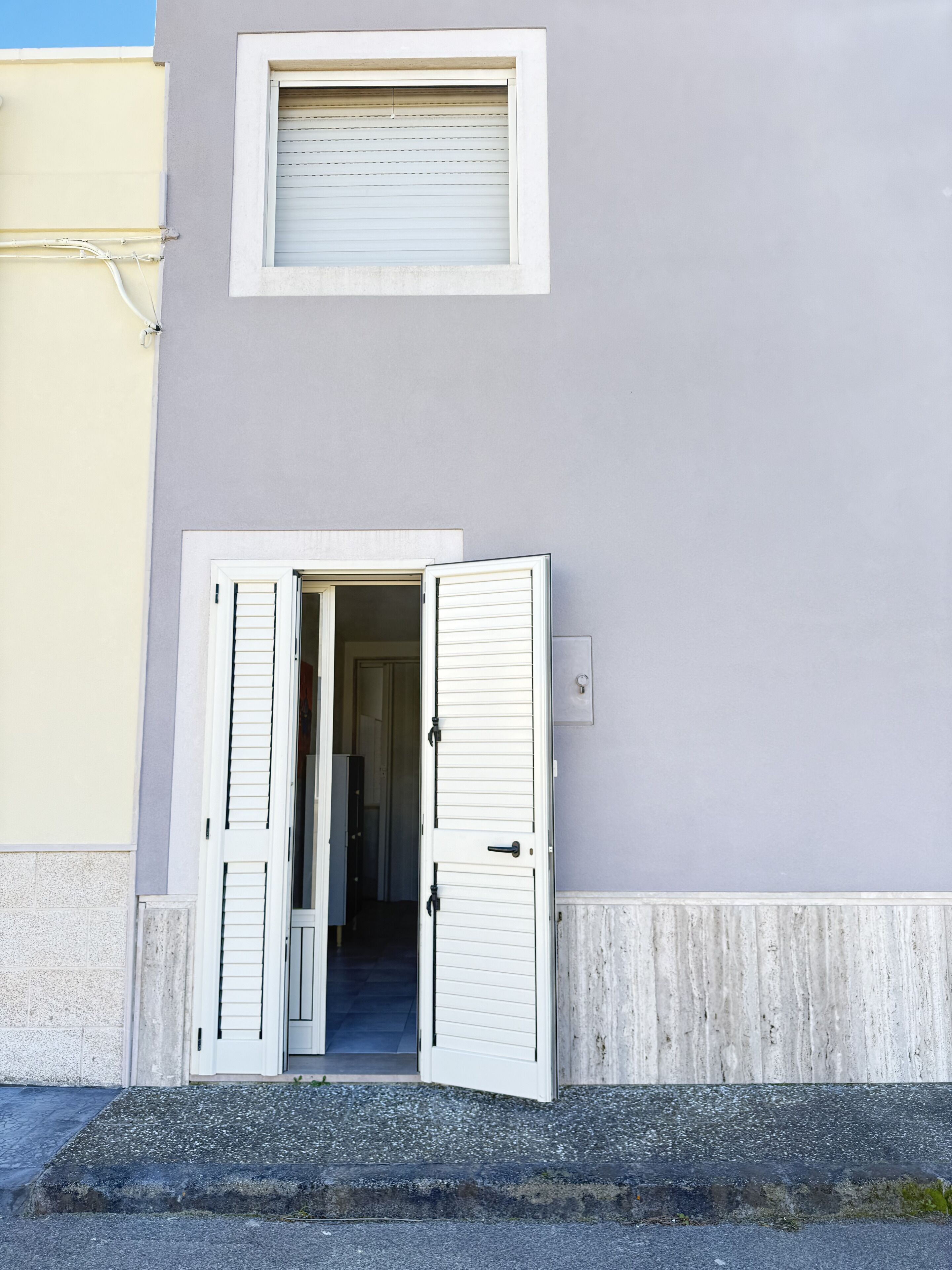 A building with a white door and window, a concrete base, and a grey wall.