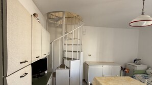 A compact kitchen with a built-in refrigerator, a small dining table, and a spiral staircase. - Bonomi vacation home 15 meters from the beach (Porto Cesareo)