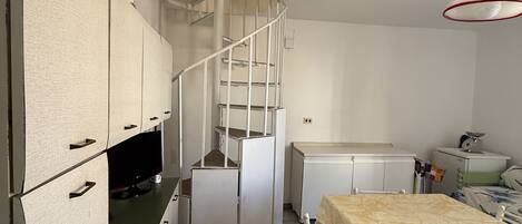 Une cuisine compacte dotée d’un réfrigérateur encastré, d’une petite table à manger et d’un escalier en colimaçon.