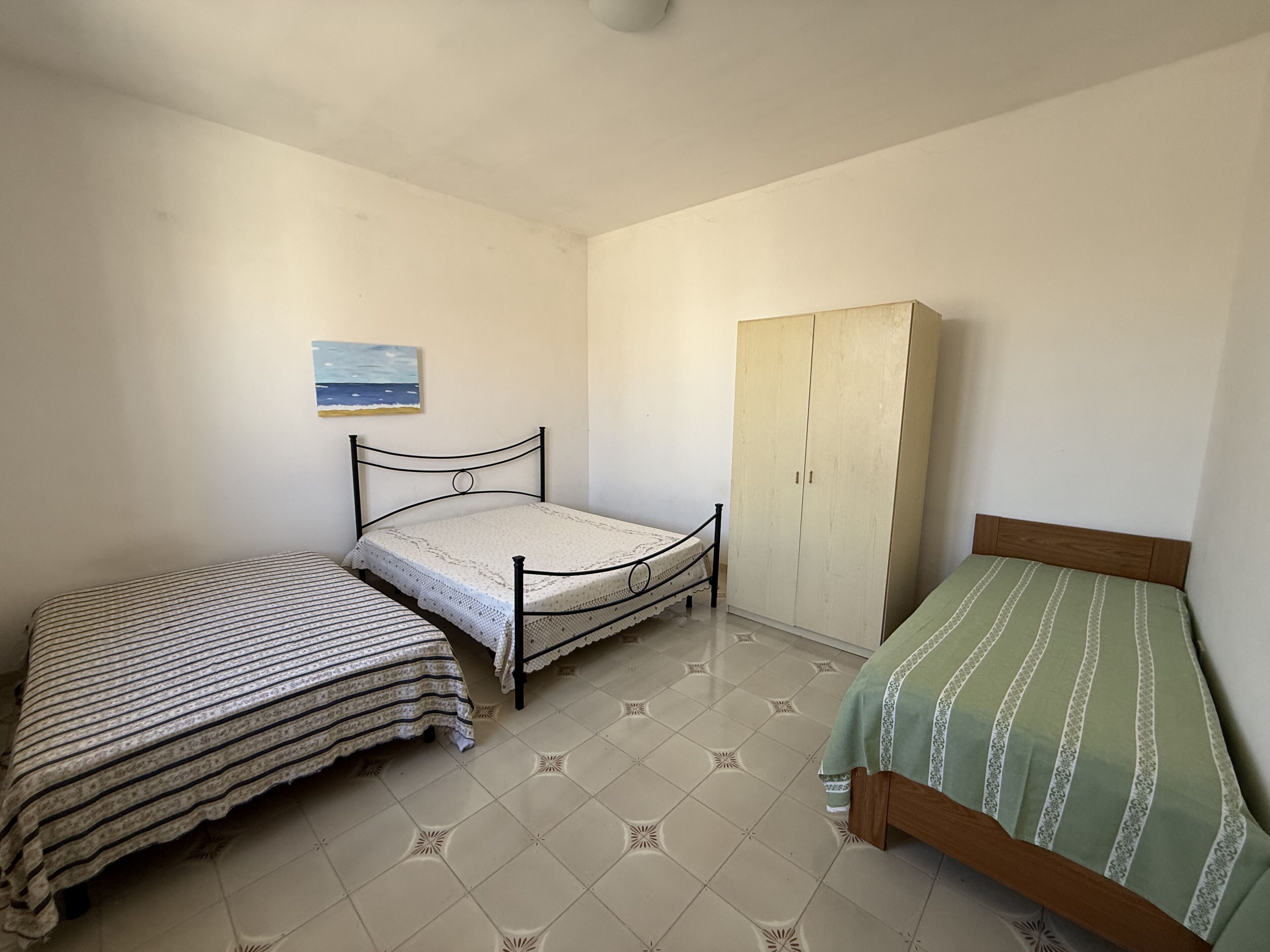 A bedroom with two single beds, a wardrobe, and a painting on the wall.