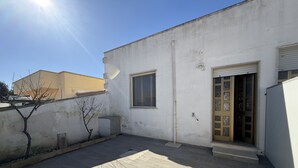 Un bâtiment à l’extérieur blanc, avec une petite fenêtre, une porte dotée de vitres décoratives et une terrasse carrelée.
