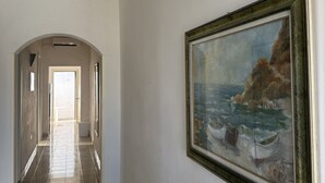 Un couloir doté d’un sol carrelé, d’un tableau représentant des bateaux sur une falaise et d’une porte en arc de cercle.