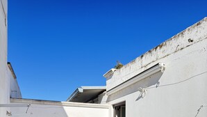 Un petit patio clos, avec une table blanche et deux chaises, une chaise rouge, et une porte donnant sur un espace intérieur.