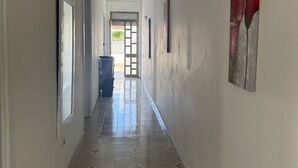Un corridoio con pavimento piastrellato, una porta a sinistra e un grande quadro a destra.