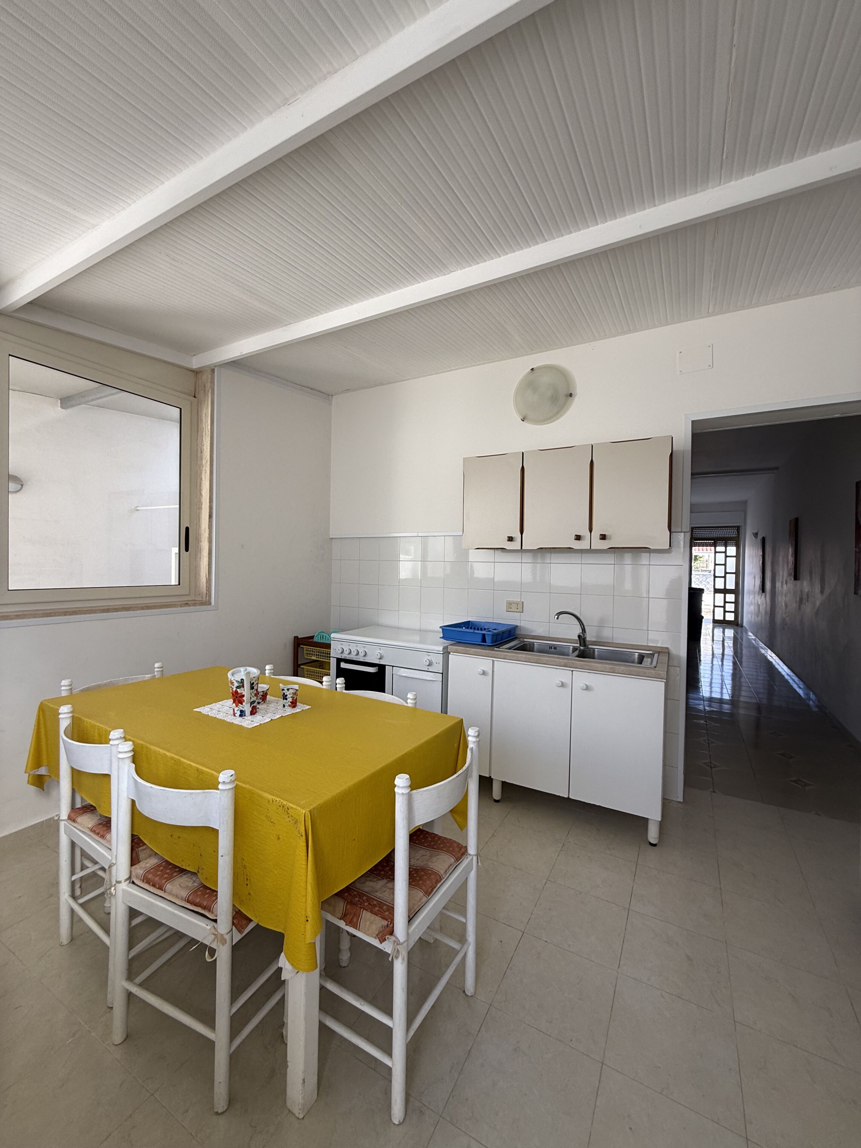 A kitchen with white cabinets, a dining table with a yellow tablecloth, and a window with a view.