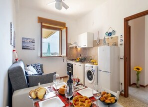 Un espacio habitable compacto con comedor, kitchenette y vista al mar a través de una ventana.