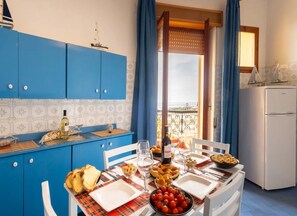 A dining area with a table set for two, blue cabinets, a refrigerator, and a view of the sea. - Sunset apartment with balcony (Porto Cesareo)