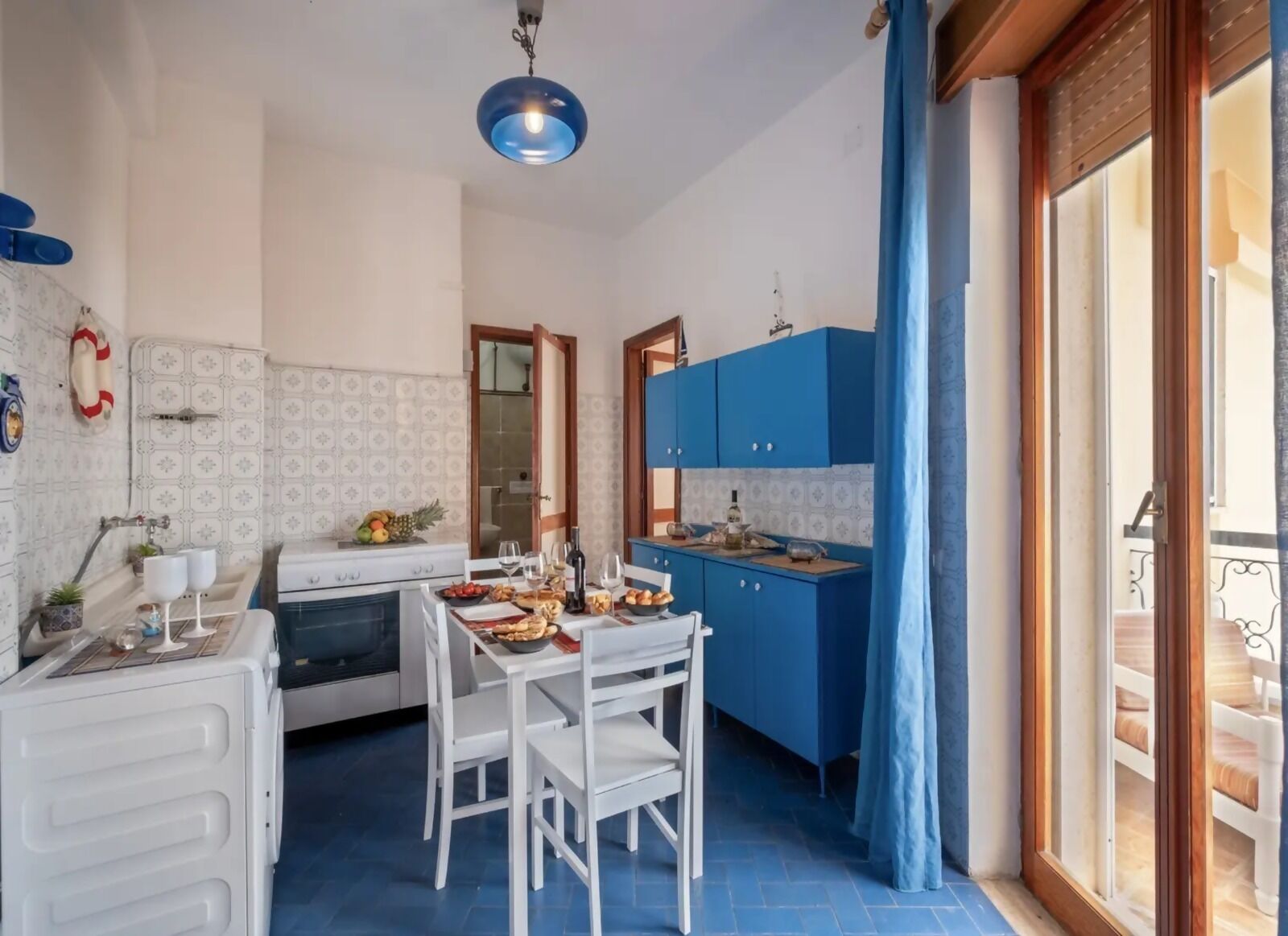 Una cucina compatta con tavolo, sedie, piano cottura e mobili azzurri.