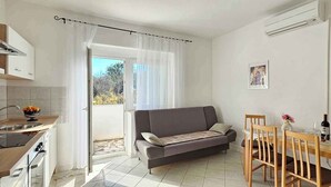 A compact living space with a kitchenette, a sofa, a dining table with chairs, and a sliding glass door leading to an outdoor area. - Holiday flat with balcony (Šilo)