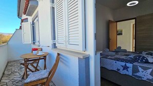 A balcony with a table and chairs, a bed with a star-patterned bedspread, and a window with shutters. - Holiday flat with balcony (Šilo)